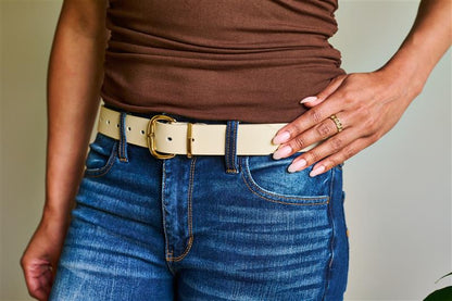 Person wearing a brown shirt, blue jeans, and a beige belt with a neutral background